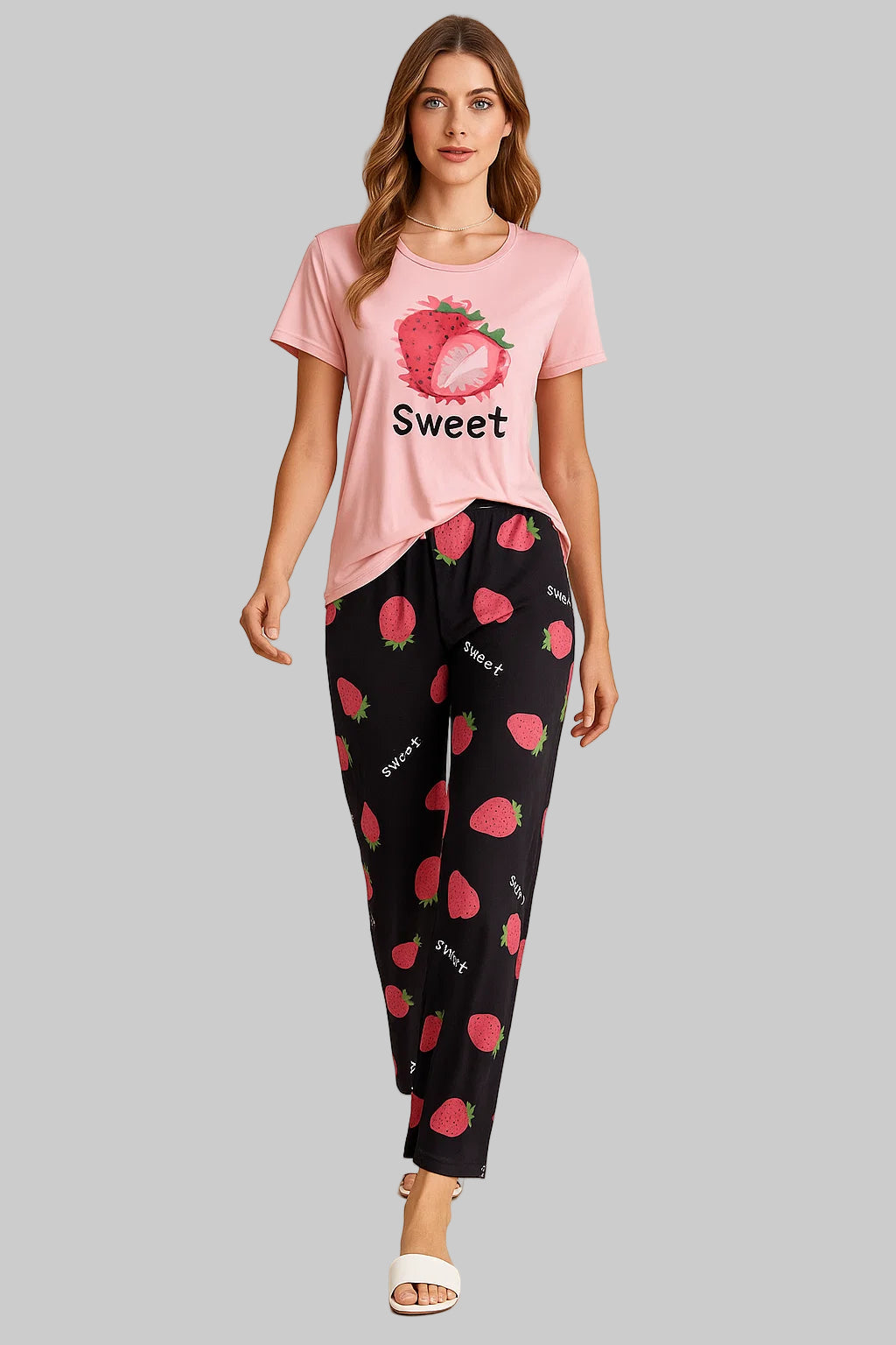 Woman wearing a pink t-shirt with strawberry design and 'Sweet' text, paired with black pants with red strawberry pattern on a beige background.