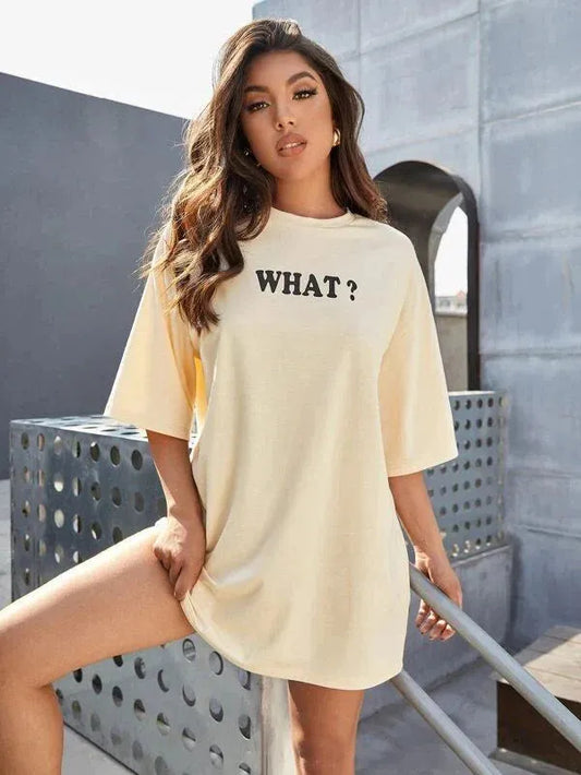 Woman wearing a beige oversized t-shirt with 'WHAT?' text outdoors.